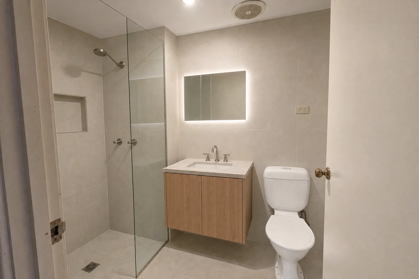 The same ensuite renovated, with floor-to-ceiling tiling, a walk-in shower and a wall-hung vanity in the same footprint