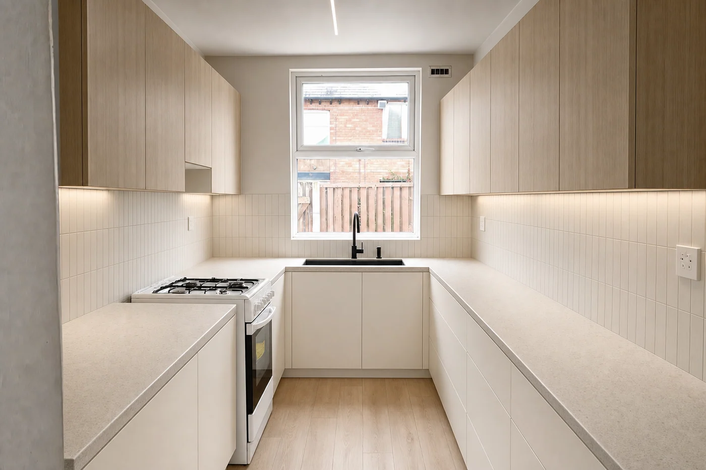 The same galley kitchen renovated, with new cabinetry, benchtop and splashback along both existing runs