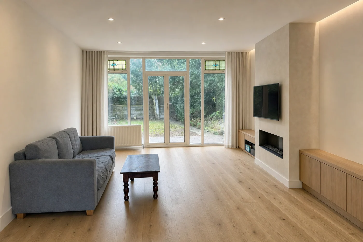 The same living room renovated, with a new timber floor, a full-height plaster fireplace wall and built-in joinery — the sofa and coffee table unchanged